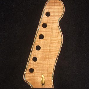 May include: Close-up of a light-colored electric guitar neck with six tuning peg holes. The neck has a decorative edge and a gold-colored accent. The text "Bruce Wei Electric Guitar Neck GN-2117" is visible.