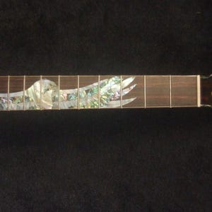 May include: A dark brown electric guitar neck with a decorative inlay of a bird in flight. The fretboard has silver frets. The headstock has six tuning peg holes. The text "Bruce Wei Electric Guitar Neck GN-2106" is at the bottom.