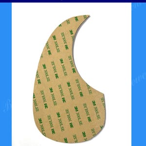 Puede incluir: Un golpeador de guitarra para una guitarra Martin D45. El golpeador tiene forma de l&aacute;grima con un respaldo adhesivo marr&oacute;n. El texto "3M 300LSE" est&aacute; impreso repetidamente en el adhesivo. La imagen tambi&eacute;n incluye el texto "Bruce Wei Musical Instruments Workshop".