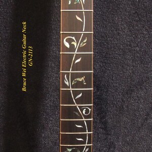 May include: Close-up of a guitar neck with a dark wood finish. The fretboard features an inlaid floral design in white and iridescent green. The text "Bruce Wei Electric Guitar Neck GN-2113" is printed on the left side.