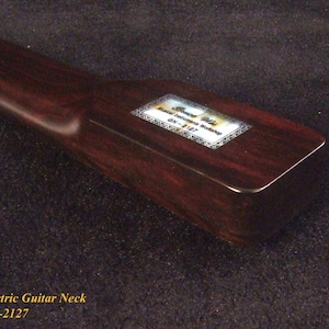 May include: A dark brown wooden electric guitar neck with a smooth finish. A rectangular label is affixed to the heel, featuring the text Bruce Wei Guitar Workshop and the model number GN-2127, surrounded by a decorative border pattern.