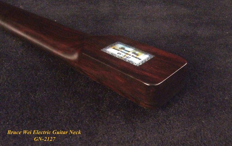 May include: A dark brown wooden electric guitar neck with a smooth finish. A rectangular label is affixed to the heel, featuring the text Bruce Wei Guitar Workshop and the model number GN-2127, surrounded by a decorative border pattern.