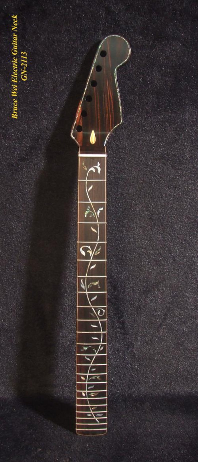 May include: A dark brown electric guitar neck with a decorative floral inlay. The headstock has tuning peg holes and a mother-of-pearl inlay. The text "Bruce Wei Electric Guitar Neck GN-2113" is visible.