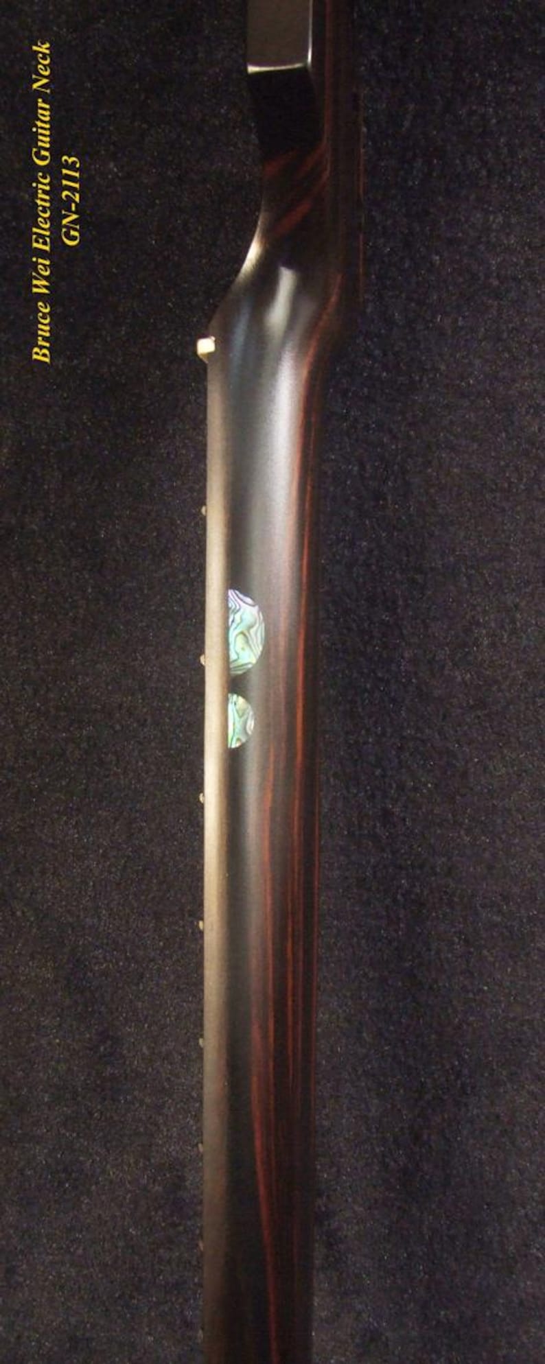 May include: Close-up of an electric guitar neck with a dark wood grain finish. The neck has two decorative inlays and the text "Bruce Wei Electric Guitar Neck GN-2113" in yellow.