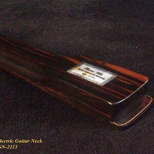 May include: A close-up of a Bruce Wei electric guitar neck, model GN-2113. The neck is made of dark wood with reddish-brown and black grain patterns. A rectangular label with text is visible.