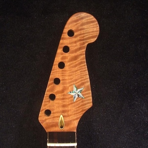 Op de afbeelding: Close-up van een houten elektrische gitaarhals met een sterinleg. De hals heeft een lichtbruin, golvend houtnerfpatroon. De kop heeft zes ronde gaten en een decoratieve ster. De tekst "Bruce Wei Electric Guitar Neck GN-2113" is zichtbaar.