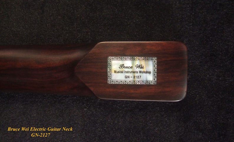 May include: A dark brown wooden electric guitar neck featuring a rectangular mother-of-pearl inlay on the heel. The inlay is engraved with the text Bruce Wei, Musical Instruments Workshop, and the model number GN-2127 in a decorative border.