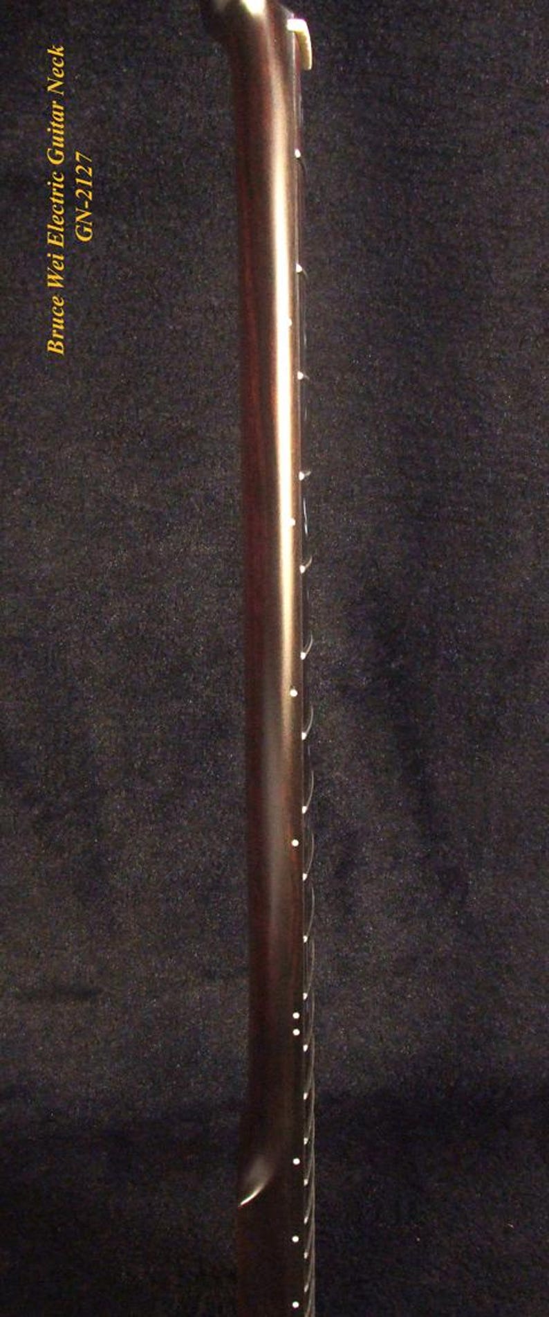May include: A dark brown electric guitar neck featuring a smooth fretboard with white dot position markers along the side. The text Bruce Wei Electric Guitar Neck GN-2127 is printed in yellow on the left side of the guitar neck component.