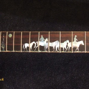 Op de afbeelding: Elektrische gitaarhals met een woestijnsc&egrave;ne-inleg. De inleg bevat een rode hoed, cactussen, cowboys te paard en honden. De toets is donkerbruin met witte inlays en gouden frets. De tekst "Bruce Wei Electric Guitar Neck GN-2113" staat onderaan.