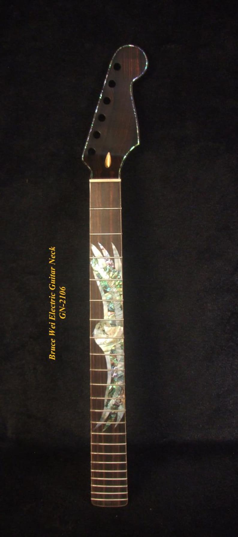 May include: A dark brown electric guitar neck with a decorative inlay. The neck has a headstock with tuning pegs and a fretboard with inlaid mother-of-pearl designs. The text "Bruce Wei Electric Guitar Neck GN-2106" is visible.