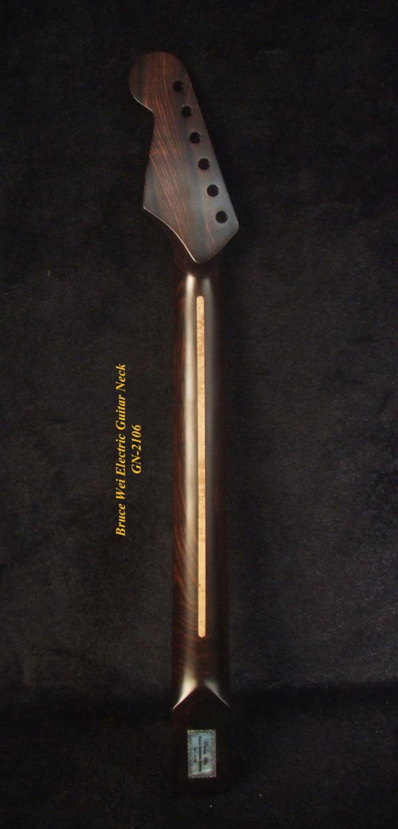 May include: Close-up of an electric guitar neck with a dark wood grain finish. The headstock has six tuning peg holes. The text "Bruce Wei Electric Guitar Neck GN-2106" is printed on the neck.