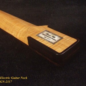 May include: Close-up of a maple electric guitar neck with a dark brown heel. The neck has a light-colored, patterned wood grain. A rectangular label with text is affixed to the heel. The text at the bottom reads "Bruce Wei Electric Guitar Neck GN-2117".