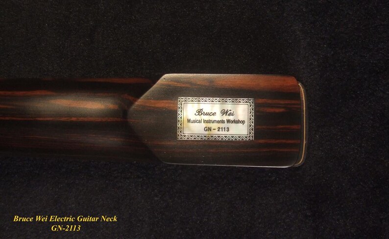 May include: A close-up of a dark brown electric guitar neck with a rectangular inlay. The inlay reads "Bruce Wei Musical Instruments Workshop GN-2113" within a decorative frame. The wood grain is visible.