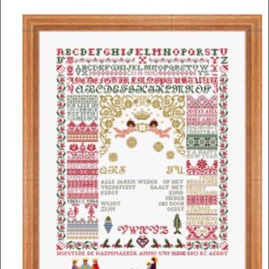 Op de afbeelding: Een ingelijst kruissteekpatroon met een witte achtergrond en kleurrijke borduurwerk. Het patroon toont een kerstscène met engelen, een ster en de tekst "Christmas 1995-1".
