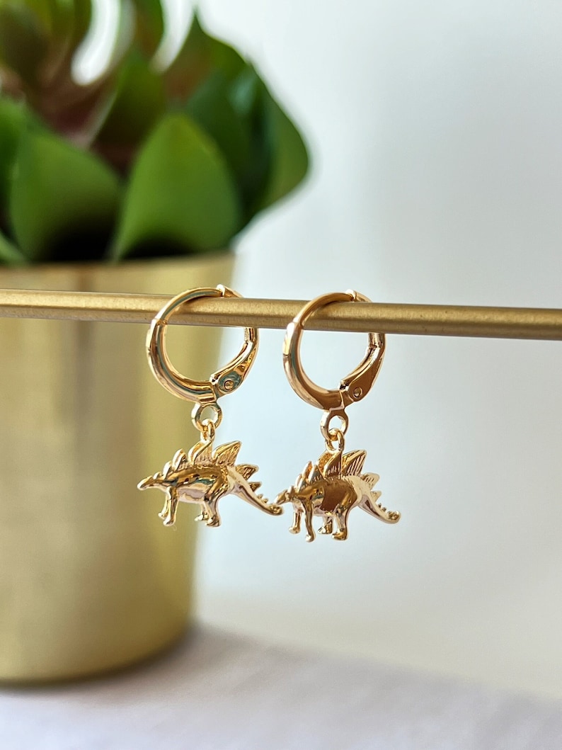 Op de afbeelding: Gouden creolen met een klein dinosaurusbedeltje aan elke creool.
