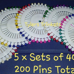 May include: Five sets of 40 colourful sewing pins, each set in a white plastic circular holder with a pearl-like trim. The text "5 x Sets of 40" and "200 Pins Total" is printed below the holders.