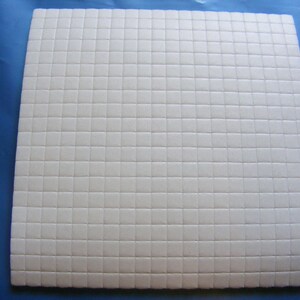 May include: A white sheet of adhesive-backed foam with a grid pattern. The foam is designed for crafts and DIY projects.