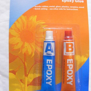 May include: Two tubes of epoxy glue, one labelled "A Resin" in blue with white lettering and the other labelled "B Hardener" in orange with white lettering. Both tubes have a 30-minute hardening time.
