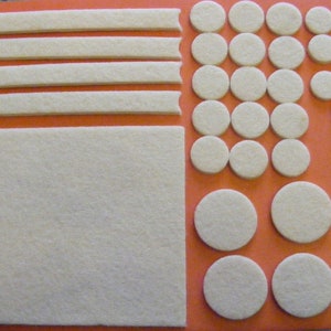 May include: A set of white felt furniture pads in various sizes and shapes. The pads are arranged on a bright orange surface. The set includes four long strips, a large square, and a variety of round pads.