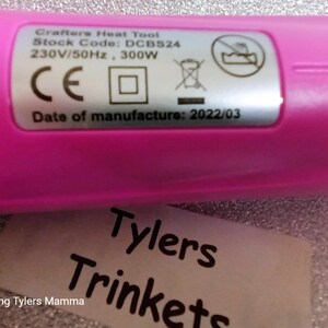 May include: A pink heat tool with a label that reads "Crafters Heat Tool", "Stock Code: DCB524", "230V/50Hz, 300W", "CE", and "Date of manufacture: 2022/03".
