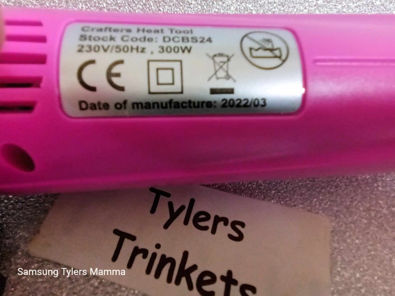 May include: A pink heat tool with a label that reads "Crafters Heat Tool", "Stock Code: DCB524", "230V/50Hz, 300W", "CE", and "Date of manufacture: 2022/03".