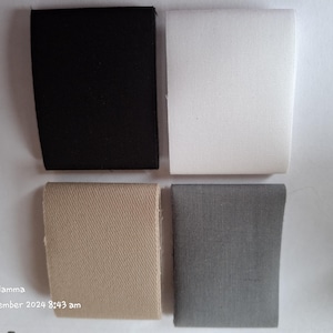 May include: Four fabric swatches in different colours and textures. The swatches are arranged in a grid pattern. The top left swatch is black, the top right swatch is white, the bottom left swatch is beige, and the bottom right swatch is grey.