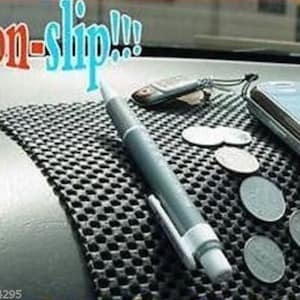 May include: A black non-slip mat with a grid pattern. A white pen, a silver phone, and several silver coins are on the mat. The text "non-slip!!!" is in the top left corner of the image.