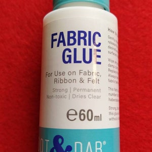 May include: A white bottle of fabric glue with a blue label that says "Fabric Glue" and "Dot & Dab". The bottle is 60 ml and is for use on fabric, ribbon, and felt. It is strong, permanent, non-toxic, and dries clear.