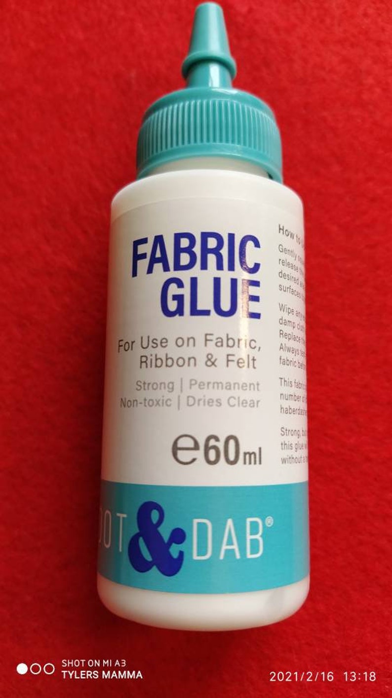 May include: A white bottle of fabric glue with a blue label that says "Fabric Glue" and "Dot & Dab". The bottle is 60 ml and is for use on fabric, ribbon, and felt. It is strong, permanent, non-toxic, and dries clear.