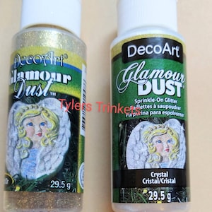May include: Two bottles of DecoArt Glamour Dust sprinkle-on glitter. The bottles are labelled with the product name and have a picture of an angel on the front. The bottles are 29.5 grams each.