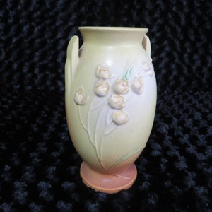 May include: A yellow and white ceramic vase with a floral design. The vase has two handles and a rounded base.