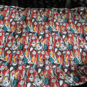 May include: A black tote bag with a repeating pattern of Jack Skellington and Sally from the Nightmare Before Christmas. The characters are in various poses and colors, including red, blue, green, and yellow.