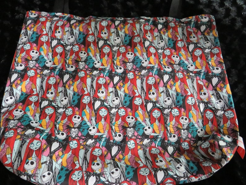 May include: A black tote bag with a repeating pattern of Jack Skellington and Sally from the Nightmare Before Christmas. The characters are in various poses and colors, including red, blue, green, and yellow.