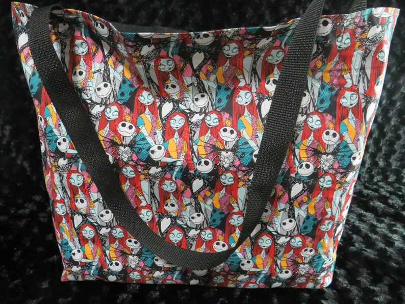 May include: A black tote bag with a colorful print of Jack Skellington and Sally from the Nightmare Before Christmas. The bag has two black straps.