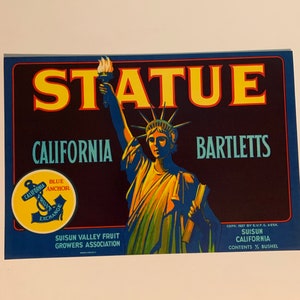 May include: A vintage fruit crate label with the Statue of Liberty, the word "STATUE" in yellow, and text for "CALIFORNIA" and "BARTLETTS". It features a "BLUE ANCHOR" logo. The label is predominantly dark blue and yellow.