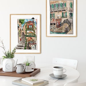 May include: Two watercolor paintings of buildings in Venice, Italy. The first painting shows a narrow street with a staircase leading up to a building with a red door and green plants. The second painting shows a canal with a bridge and a building with a sign that says "Galle Lavoro".