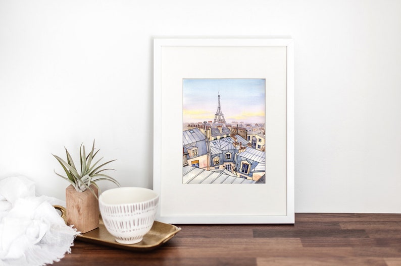 May include: A watercolor painting of a Parisian cityscape with the Eiffel Tower in the distance. The painting features a view of rooftops and buildings in shades of blue and gray.