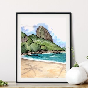 May include: Watercolor painting of a beach scene with a mountain in the background. The beach is sandy with palm tree shadows and the water is blue. The mountain is green and brown.