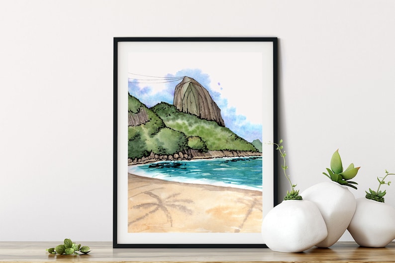 May include: Watercolor painting of a beach scene with a mountain in the background. The beach is sandy with palm tree shadows and the water is blue. The mountain is green and brown.