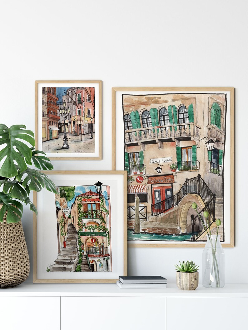 May include: Three framed watercolor paintings of Italian cityscapes. The paintings depict narrow streets, buildings with colorful facades, and charming details like balconies, stairs, and streetlights.