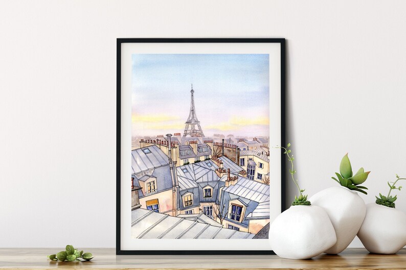 May include: A watercolor painting of a Parisian cityscape with the Eiffel Tower in the background. The painting depicts a view from a rooftop, showing the rooftops of buildings with chimneys and windows. The sky is a light blue with a hint of pink in the distance.