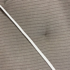 May include: A diagonal view of a white elastic band against a textured, brown fabric background. The elastic band is thin and appears to be made of woven material. The fabric has a woven pattern.