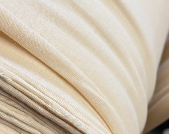 May include: Close-up of a cream-colored fabric rolled up. The fabric has a smooth, slightly textured surface.