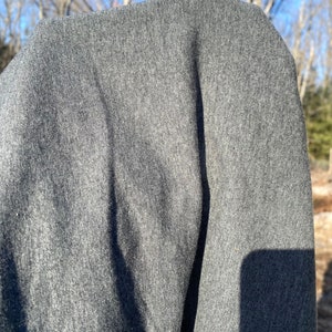 May include: A close-up shot of a gray fabric, possibly a sweatshirt or sweater. The material appears soft and textured, with subtle variations in tone. The lighting suggests an outdoor setting.