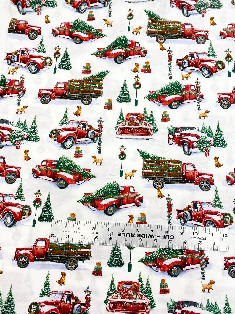 K&ouml;nnte beinhalten: Wei&szlig;er Stoff mit einem sich wiederholenden Muster aus roten Oldtimer-Trucks, die Weihnachtsb&auml;ume, Geschenke und kleine braune Hunde transportieren. Gr&uuml;ne Weihnachtsb&auml;ume und Stra&szlig;enlaternen sind ebenfalls abgebildet.