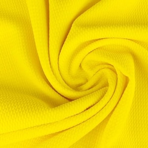 May include: Bright yellow fabric with a textured, dimpled surface. The material is draped and folded, creating soft curves and shadows. The fabric's color is a vibrant, sunny yellow.