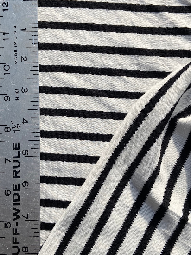 May include: Black and white striped fabric with a ruler measuring 12 inches. The fabric is a soft, stretchy knit.