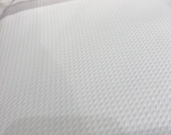 May include: Close-up of white fabric with a textured, diamond-shaped pattern. The fabric appears to be folded, with a smooth, plain white fabric visible in the background. The texture suggests a possible athletic or performance material.