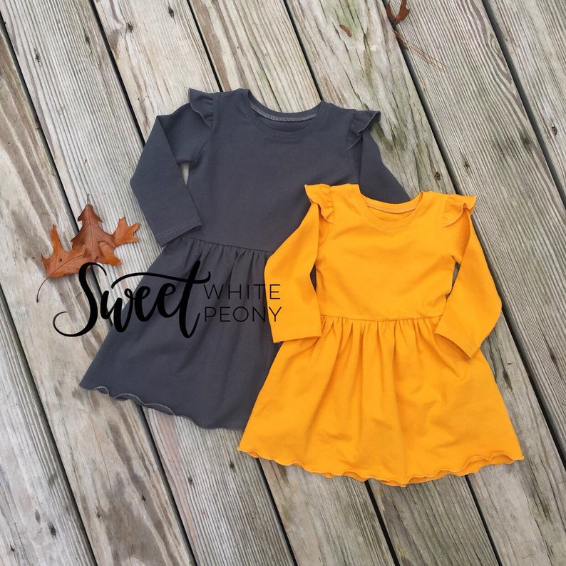 May include: Two long-sleeved dresses with ruffled sleeves. One dress is gray and the other is yellow. Both dresses have a gathered skirt.
