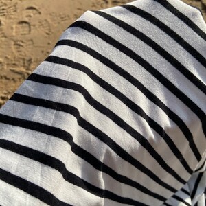 May include: Close-up of a white and black striped fabric. The fabric is soft and has a subtle sheen.